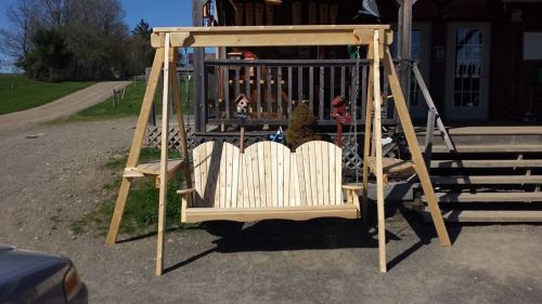 A wooden swing set with a double seat, placed outdoors near a house and grassy area.