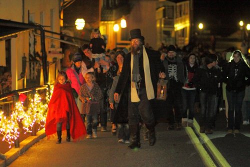 A group of people, including children, walking at night with lanterns and festive lights in a charming setting.