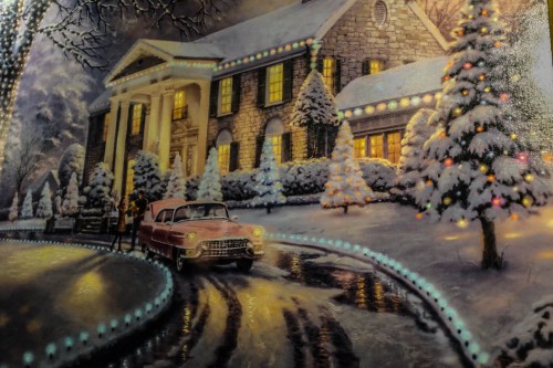 A snowy scene featuring a classic car in front of a beautifully lit house surrounded by decorated trees.