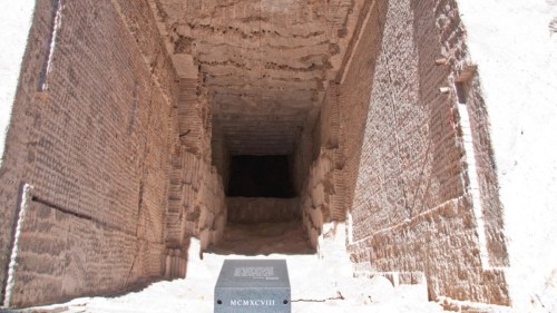 Ancient stone entrance leading into a dark chamber, with inscriptions on the walls and a stone marker in the foreground.