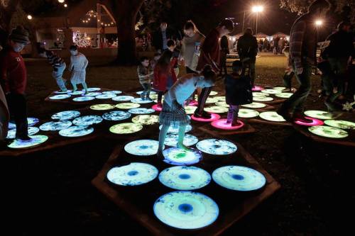 Children play on illuminated, colorful circular pads in a festive outdoor setting at night.