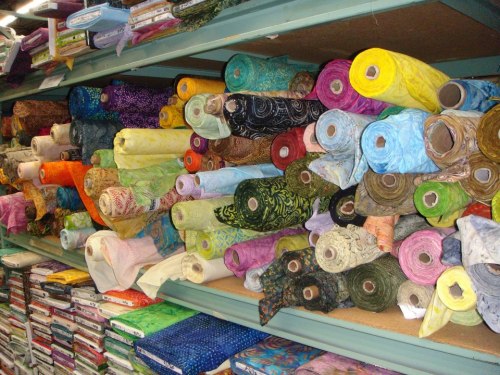 A colorful display of rolled fabric bolts stacked on shelves in a fabric store.
