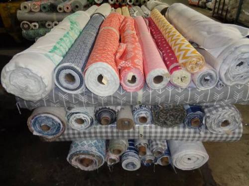 A stack of various fabric rolls in different colors and patterns, neatly arranged on shelves.