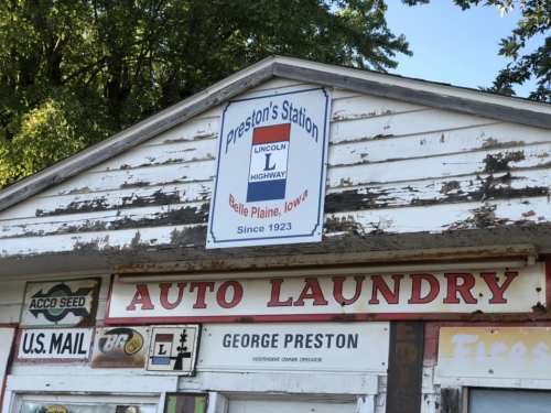 Sign for Preston's Station in Belle Plaine, Iowa, featuring "Auto Laundry" and "U.S. Mail" on a weathered building.