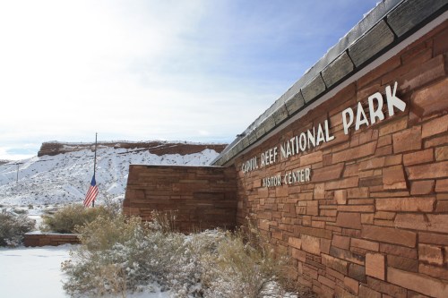 Sign for Capitol Reef National Park Visitor Center, with snow-covered landscape and a flag in the foreground.