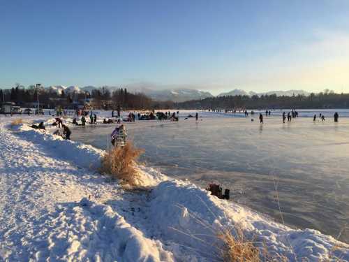 People ice skating and enjoying winter activities on a frozen lake surrounded by snow and mountains.