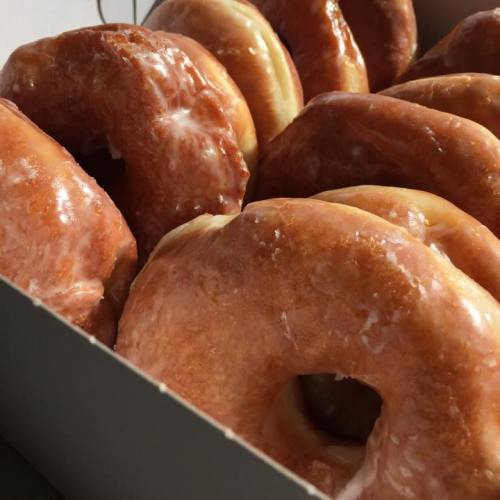 A close-up of a box filled with glazed donuts, showcasing their shiny, golden-brown surfaces.