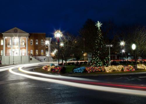 A festive town square at night, featuring a decorated Christmas tree and colorful lights around a roundabout.