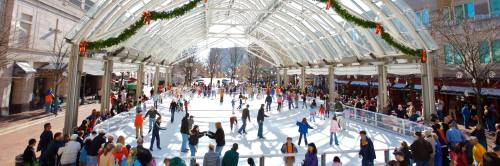A bustling ice skating rink under a glass canopy, filled with skaters and festive decorations.