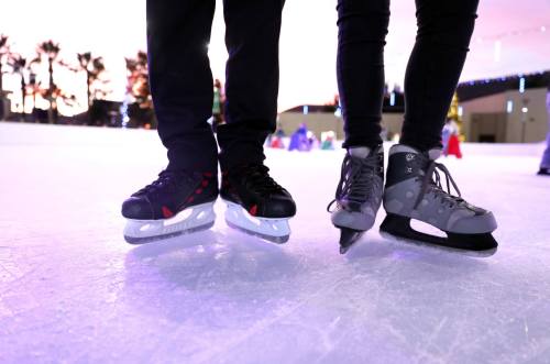 Two pairs of ice skates on an ice rink, with a colorful background and people skating in the distance.