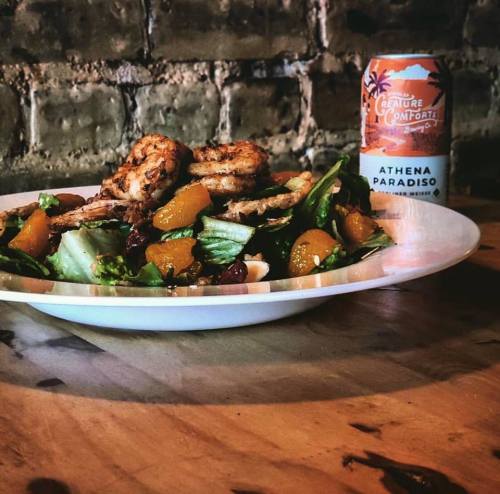 A vibrant salad with grilled chicken, mandarin oranges, and a can of Athena Paradiso beverage on a wooden table.