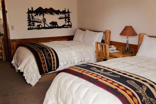Cozy hotel room with two beds, rustic decor, and a wooden table, featuring mountain-themed wall art.