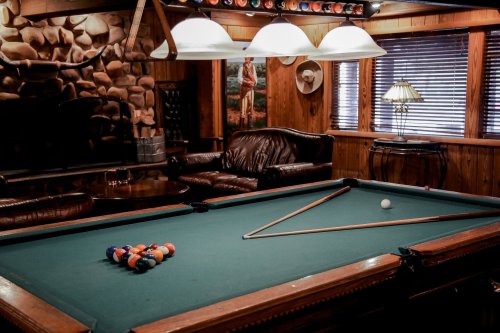 A cozy game room featuring a pool table, leather seating, and warm wooden decor.