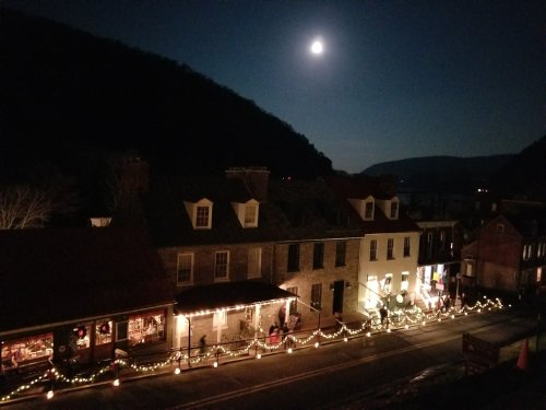 A moonlit night over a quaint town, with festive lights adorning buildings and a mountain backdrop.