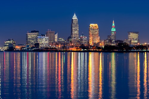Cleveland skyline at night, with colorful lights reflecting on the water.
