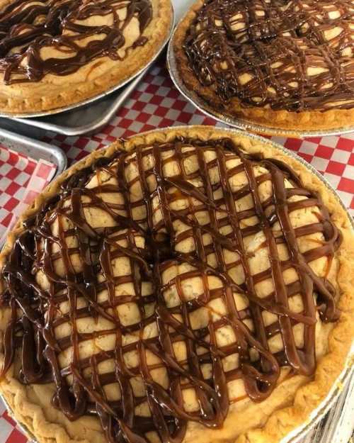 Three delicious pies with a crisscross chocolate drizzle on top, set on a red and white checkered tablecloth.