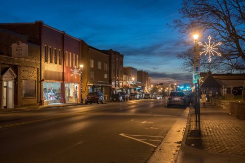 A quiet street at dusk, lined with shops and festive lights, creating a cozy, inviting atmosphere.