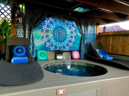 A cozy outdoor space featuring a hot tub, lounge chairs, and a vibrant mandala tapestry on the wall.
