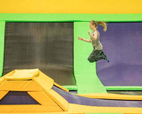 A child jumps joyfully on a trampoline at a trampoline park, surrounded by colorful padded walls.
