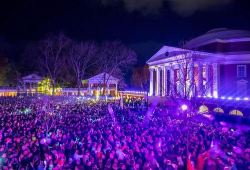 A large crowd gathers at night, illuminated by colorful lights near a historic building with columns.
