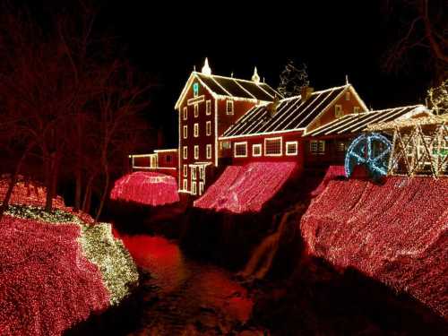 A beautifully lit house surrounded by vibrant red and white Christmas lights, reflecting in a nearby stream at night.