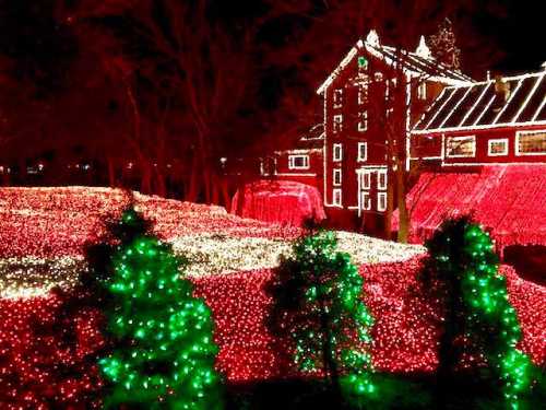 A beautifully lit landscape featuring red and green Christmas lights surrounding a large building at night.