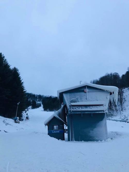 A snow-covered ski lift station surrounded by trees on a cloudy winter day.