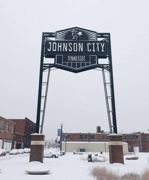 Sign for Johnson City, Tennessee, surrounded by snow-covered ground and buildings on a winter day.
