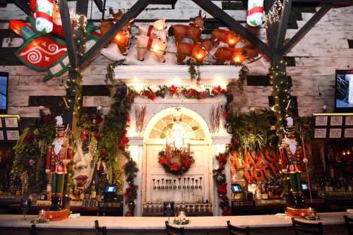 Festively decorated bar with holiday lights, greenery, and ornaments, featuring a vintage-style backdrop and festive decor.