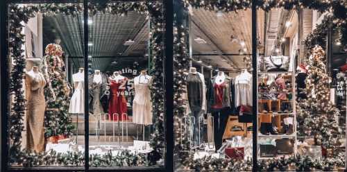 A festive store window display featuring elegant dresses and holiday decorations, showcasing a variety of clothing and accessories.