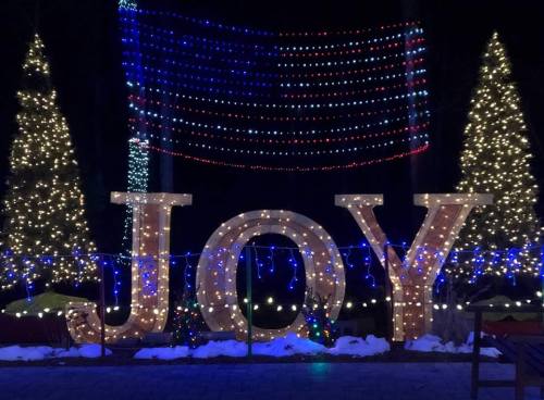 Large illuminated letters spelling "JOY" surrounded by festive lights and decorated trees.