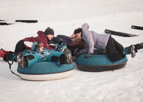 A group of children and adults enjoying snow tubing on a snowy hill, laughing and playing together.
