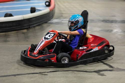 A child in a blue helmet races a red go-kart on an indoor track, focused and enjoying the ride.