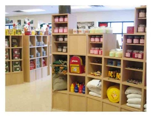 A brightly lit store interior with wooden shelves displaying jars, toys, and various packaged goods.