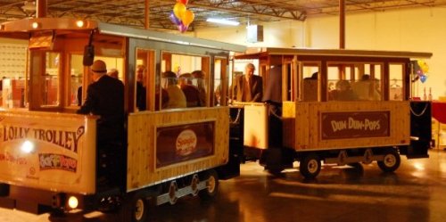 Two wooden trolleys are parked indoors, filled with people, in a festive setting with balloons and decorations.