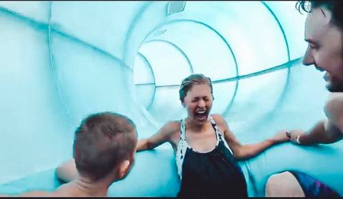 A woman and two children slide down a water slide, laughing and enjoying the ride in a bright blue tunnel.
