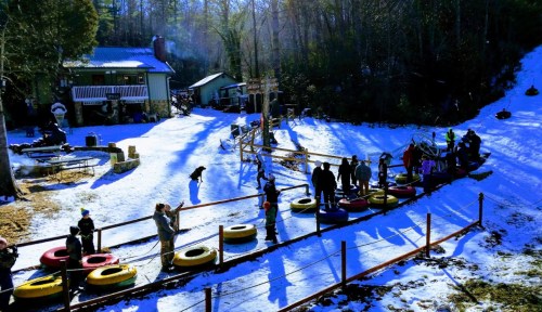 A snowy hill with people tubing, a small building in the background, and colorful inner tubes lined up for use.