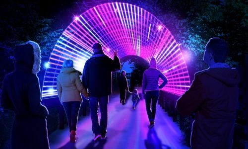 A group of people walks through a brightly lit, colorful tunnel of lights at night.