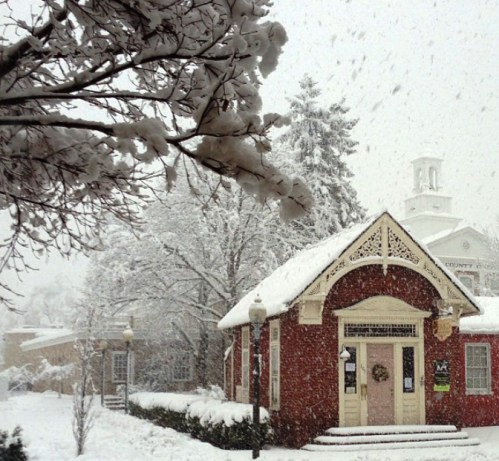 A quaint red building covered in snow, surrounded by trees, with heavy snowfall creating a winter wonderland scene.
