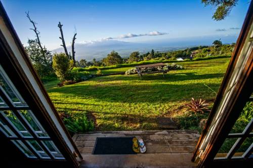 View from an open doorway overlooking a lush green landscape and distant mountains under a clear blue sky.