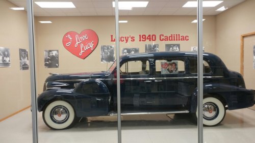 A vintage 1940 Cadillac displayed in a glass case, with a heart sign and photos on the wall behind it.