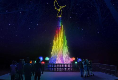 A colorful illuminated tower with a bird on top, surrounded by people admiring the display at night.