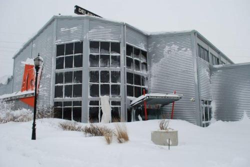 A snow-covered building with large windows, partially obscured by snowdrifts, under a gray sky.