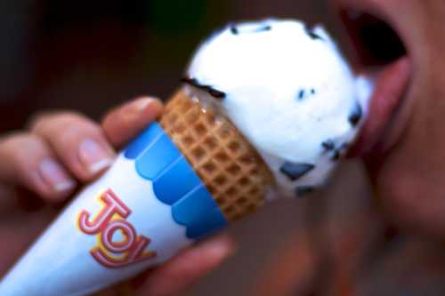 A close-up of a person about to lick a cone of ice cream topped with chocolate sprinkles.