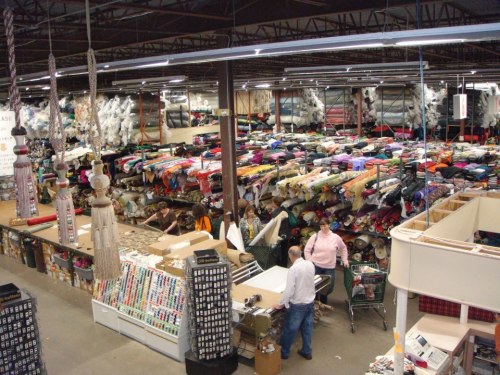 A large fabric store filled with colorful rolls of fabric, sewing supplies, and shoppers browsing the aisles.