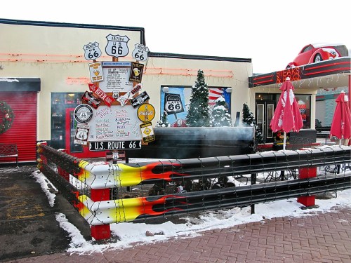 A retro diner decorated for the holidays, featuring Route 66 signs, festive trees, and a smoky grill outside.