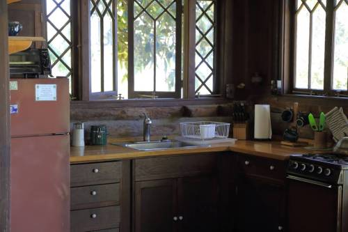 A cozy kitchen with wooden cabinets, a sink, stove, and large windows letting in natural light.