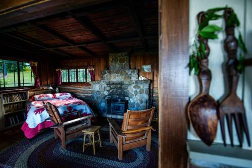 Cozy cabin interior with a stone fireplace, wooden furniture, and a bed adorned with a colorful quilt.