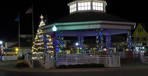 A festive gazebo decorated with colorful lights and a Christmas tree, set against a night sky.