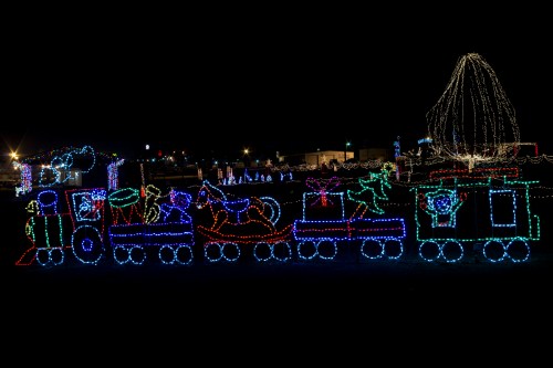Colorful holiday lights form a train with festive decorations against a dark night sky.